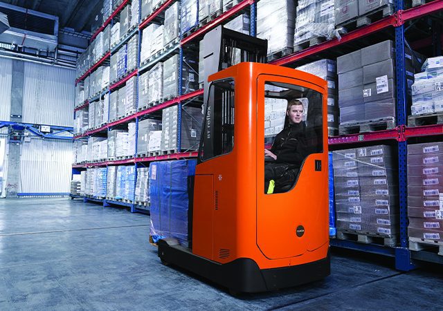 Empilhadeira retrátil laranja operando em armazém climatizado com pallets embalados, utilizada em ambientes alimentícios.