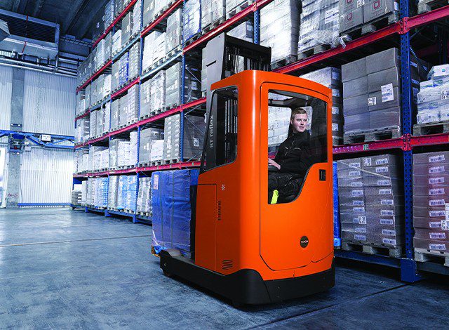 Empilhadeira retrátil laranja operando em armazém climatizado com pallets embalados, utilizada em ambientes alimentícios.