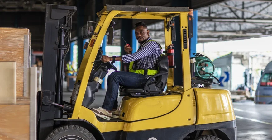 Operador conduzindo empilhadeira em ambiente industrial durante atividade logística.