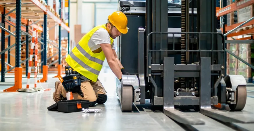 Técnico realizando manutenção em empilhadeira, simbolizando os cuidados com manutenção preventiva e corretiva em operações logísticas.