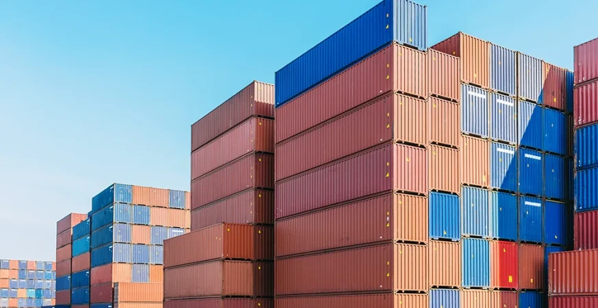 Pátio logístico com dezenas de contêineres empilhados em diferentes cores sob céu aberto.