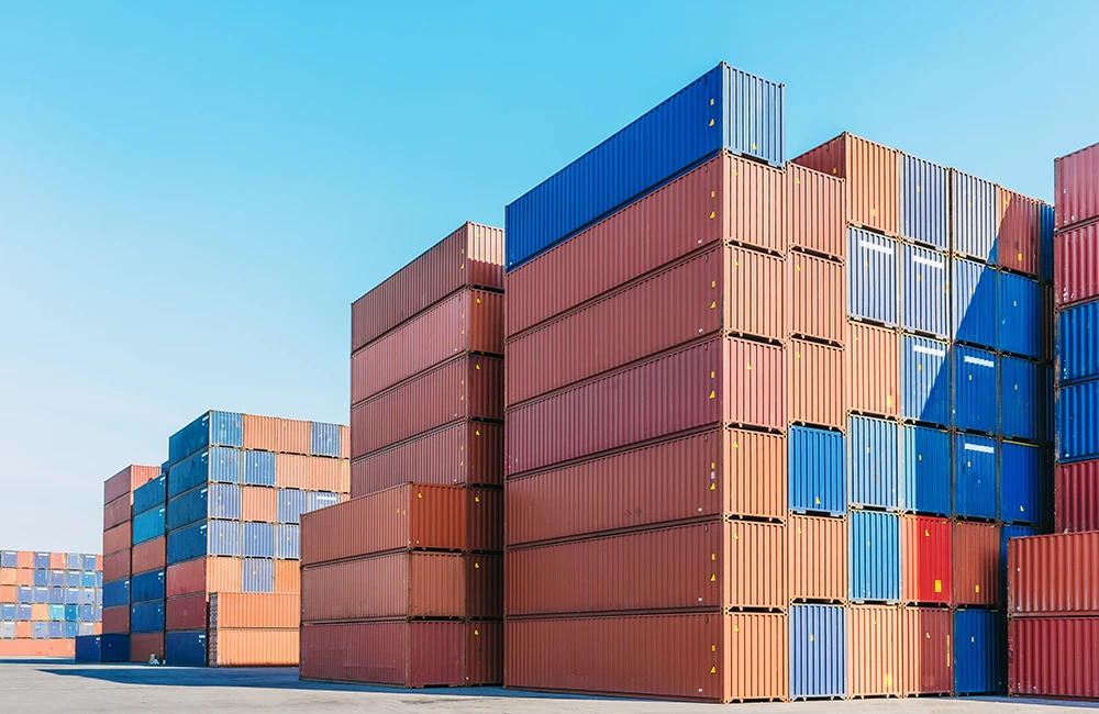 Pátio logístico com dezenas de contêineres empilhados em diferentes cores sob céu aberto.