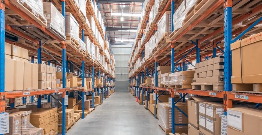 Corredor de armazém logístico com prateleiras altas e caixas organizadas em paletes.