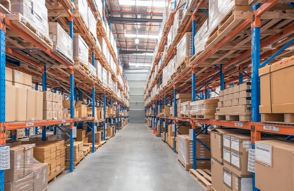 Corredor de armazém logístico com prateleiras altas e caixas organizadas em paletes.