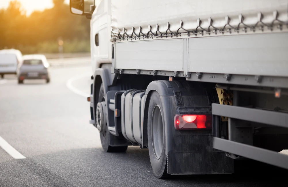 Caminhão trafegando em rodovia paulista ao entardecer, com destaque para o eixo traseiro e lanterna acesa.