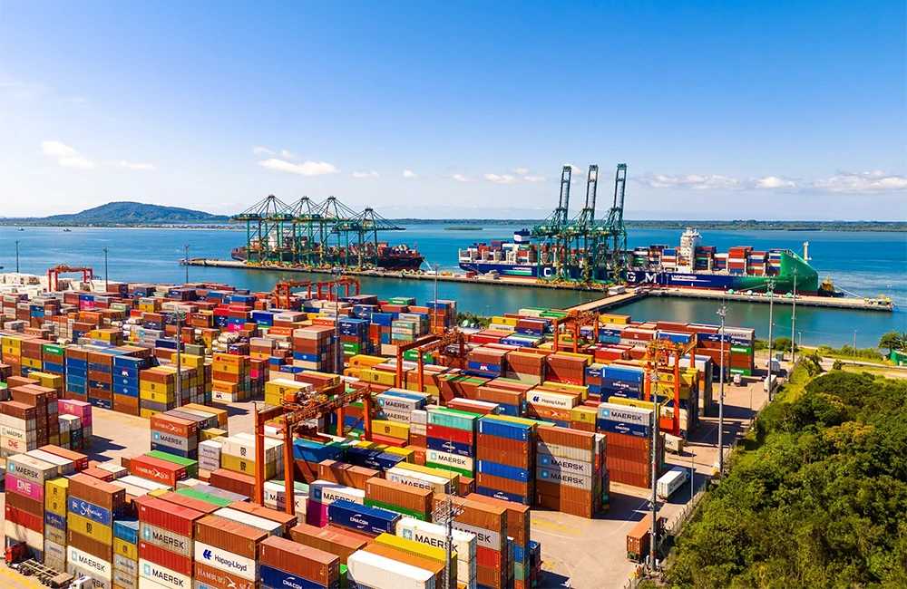 Vista aérea de terminal portuário em Santa Catarina com contêineres e guindastes à beira-mar.