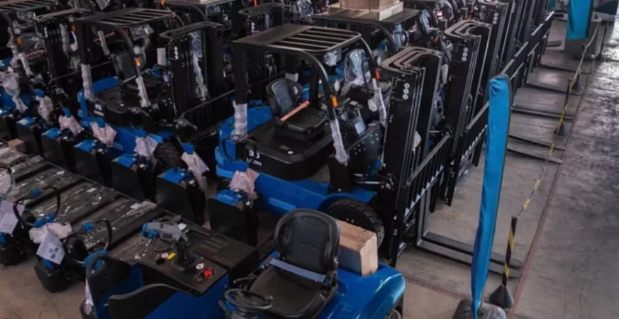 Linha de empilhadeiras novas organizadas em galpão logístico para distribuição.