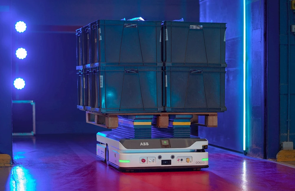 Robô móvel autônomo transportando caixas empilhadas sobre palete em ambiente industrial iluminado.