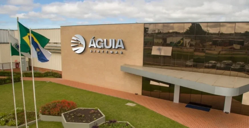Fachada da unidade industrial da Águia Sistemas, com jardim, bandeiras e entrada principal do complexo fabril.