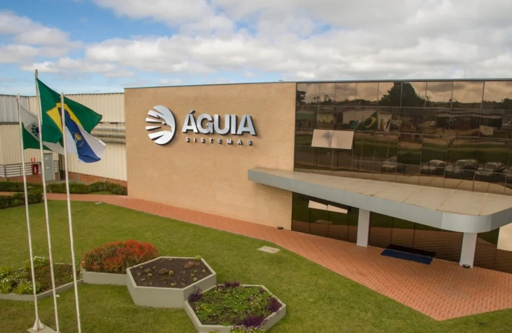 Fachada da unidade industrial da Águia Sistemas, com jardim, bandeiras e entrada principal do complexo fabril.