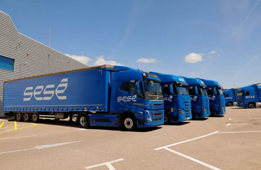 Frota de caminhões da Sesé Logística estacionada em área operacional ao lado de centro de distribuição.