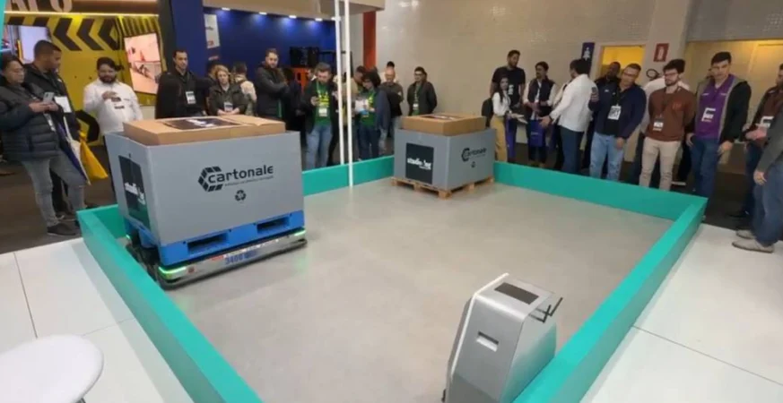 Demonstração de robôs móveis autônomos transportando cargas em área de testes durante feira de intralogística.