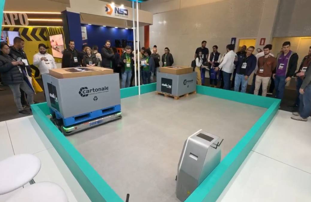 Demonstração de robôs móveis autônomos transportando cargas em área de testes durante feira de intralogística.