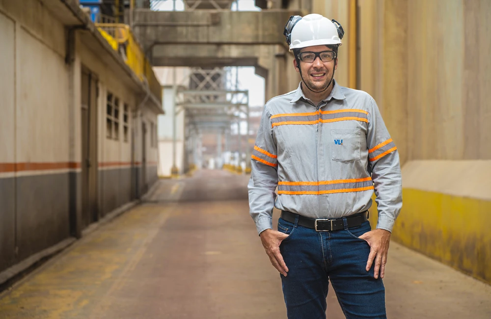 Profissional da operação ferroviária usando capacete, óculos de proteção e uniforme de segurança em área industrial.