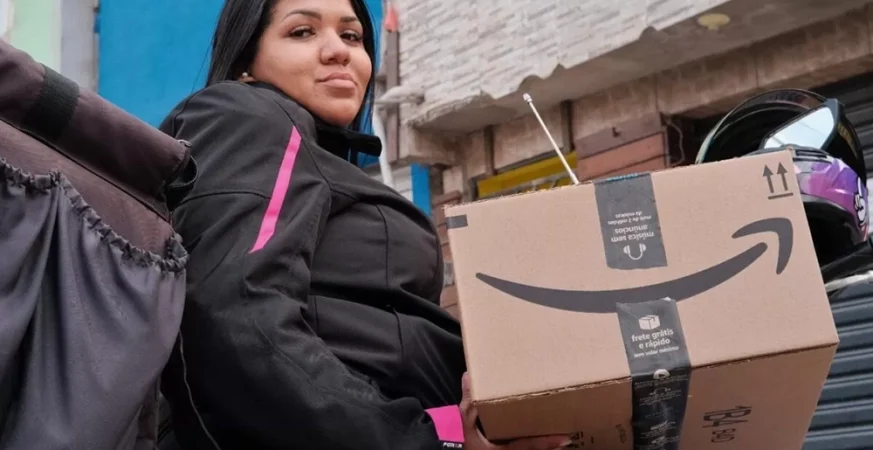 Entregadora segurando uma caixa da Amazon em área urbana, representando logística e entregas em comunidades brasileiras.