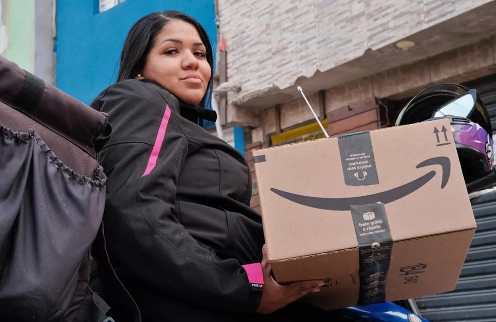 Entregadora segurando uma caixa da Amazon em área urbana, representando logística e entregas em comunidades brasileiras.