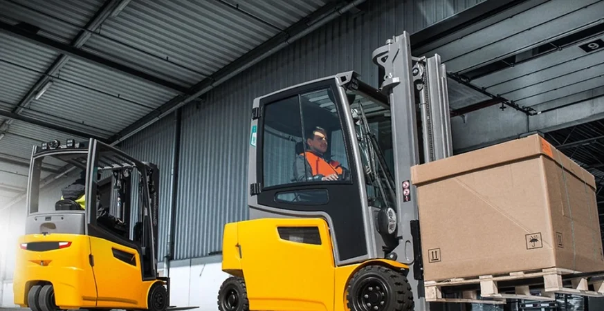 Empilhadeiras elétricas operando em galpão logístico moderno com corredores altos e operação indoor.