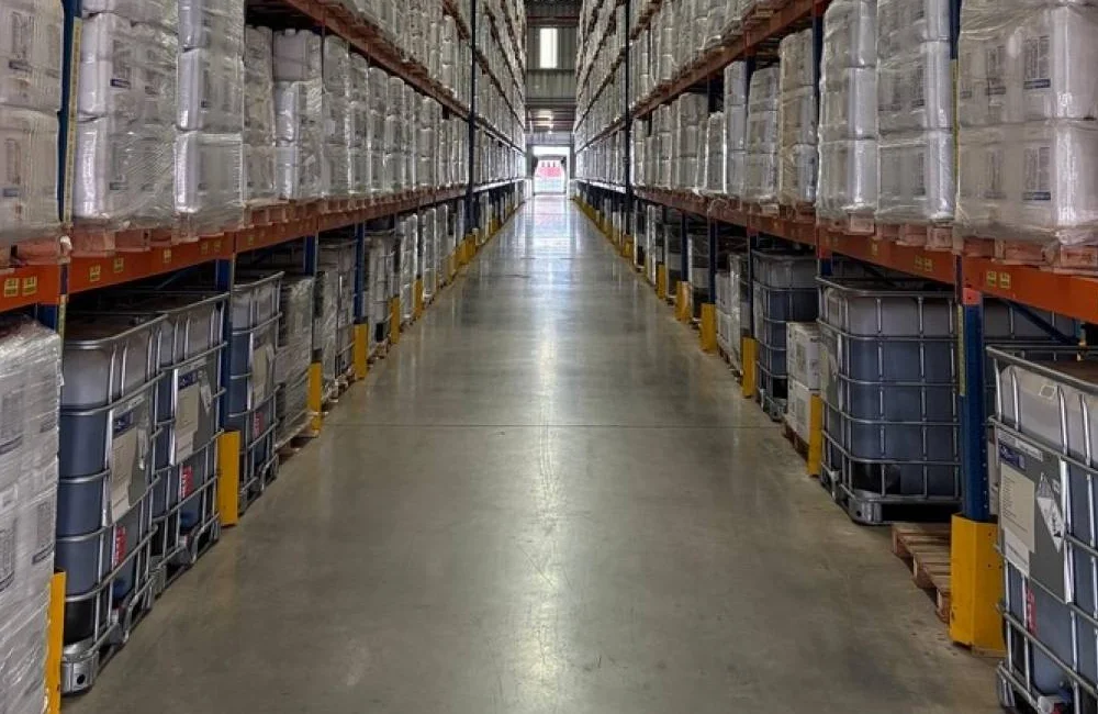 Corredor de centro logístico com paletes e contêineres organizados em estantes, ilustrando eficiência na armazenagem e gestão de estoque.