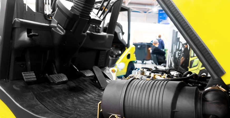 Técnico realizando manutenção em empilhadeira contrabalançada, com foco no compartimento mecânico do equipamento.