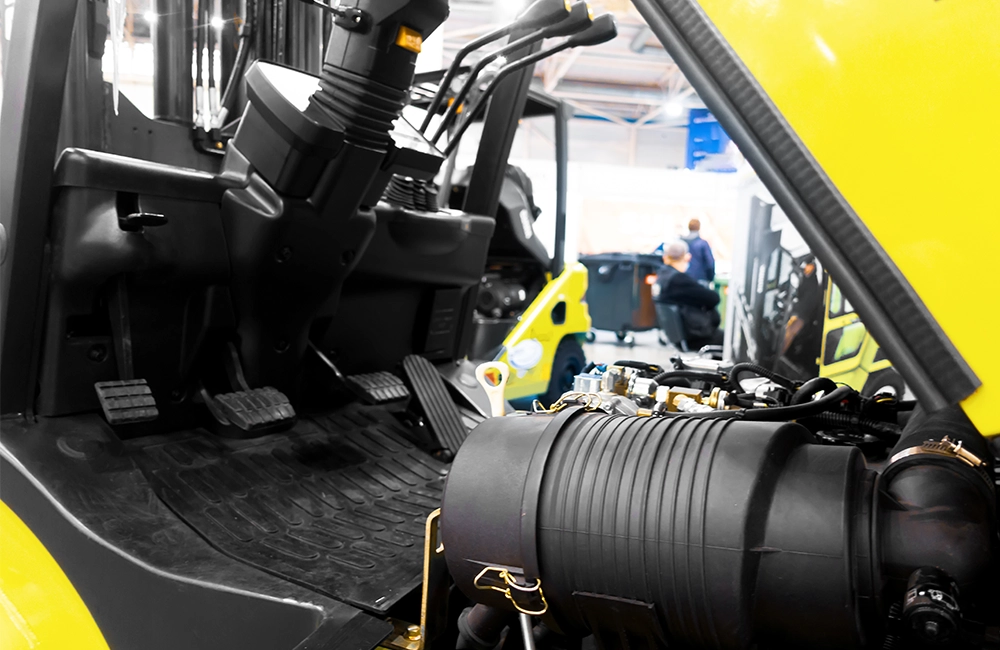 Técnico realizando manutenção em empilhadeira contrabalançada, com foco no compartimento mecânico do equipamento.