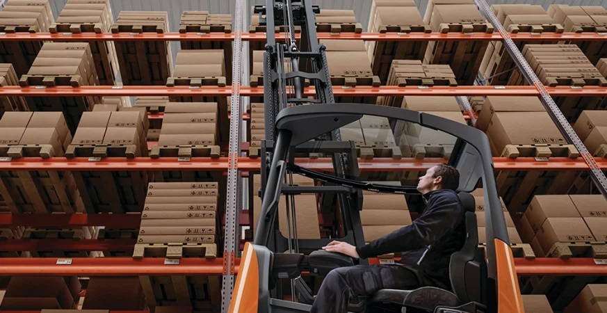 Empilhadeiras operando em dois turnos dentro de um centro de distribuição, mostrando aumento de fluxo e desgaste operacional.