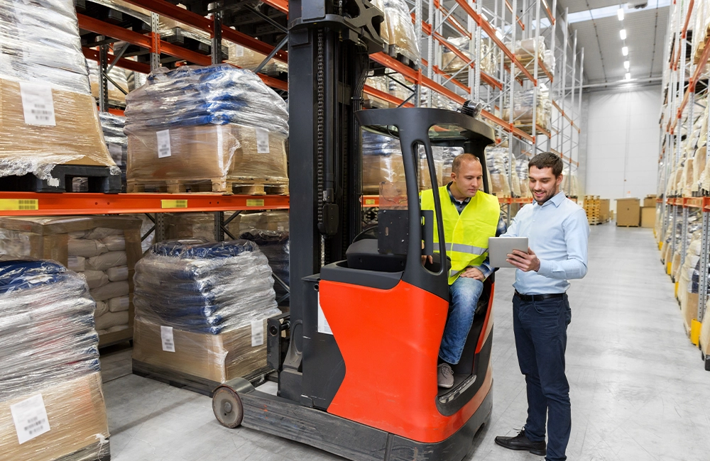 Operador utilizando dispositivo de telemetria ao lado de empilhadeira em operação dentro de centro de distribuição.