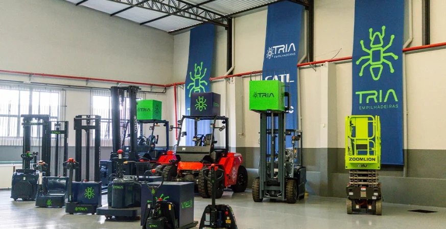 Frota de empilhadeiras e equipamentos de intralogística elétricos da Tria reunidos em galpão, destacando modelos com tecnologia de lítio.