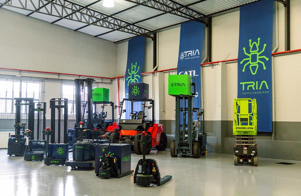 Frota de empilhadeiras e equipamentos de intralogística elétricos da Tria reunidos em galpão, destacando modelos com tecnologia de lítio.