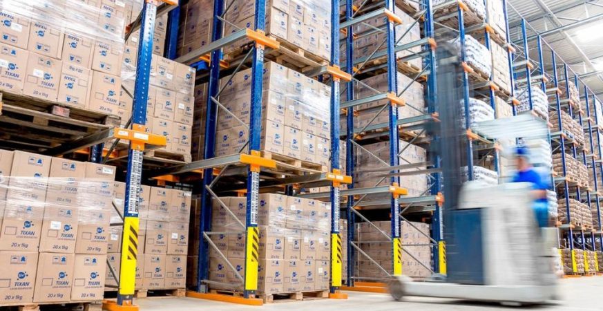 Empilhadeira operando em corredor de armazém logístico ilustrando o comparativo entre sistemas de armazenagem Drive-in e Porta Paletes.