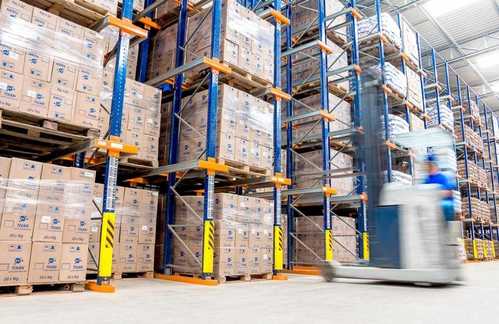 Empilhadeira operando em corredor de armazém logístico ilustrando o comparativo entre sistemas de armazenagem Drive-in e Porta Paletes.