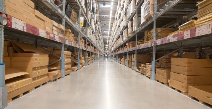 Corredor principal de um Centro de Distribuição (CD) moderno, com prateleiras cheias de caixas e um piso amplo, ilustrando o tema de gargalos logísticos ou projeto de CD.