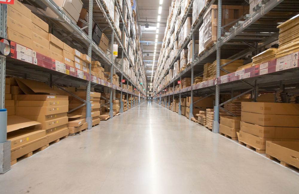 Corredor principal de um Centro de Distribuição (CD) moderno, com prateleiras cheias de caixas e um piso amplo, ilustrando o tema de gargalos logísticos ou projeto de CD.