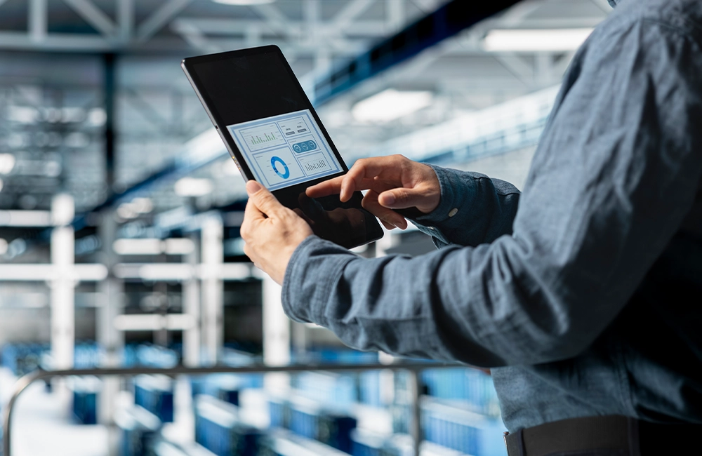 Profissional de logística operando tablet com software de gestão de transporte em armazém moderno, ilustrando a redução de 60% no tempo de montagem de carga da JCP Logística com tecnologia MáximaTech.