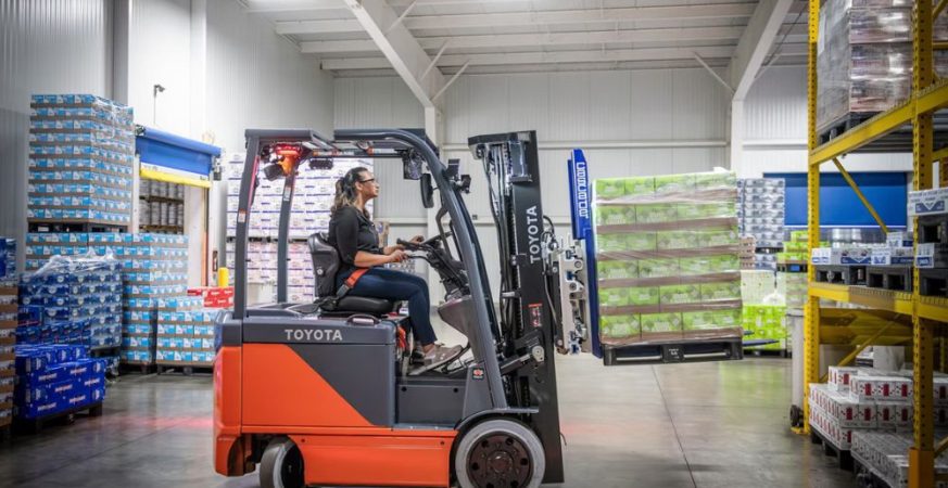 Empilhadeira circulando em corredor de armazém com pallets, ilustrando operações logísticas e custos operacionais.