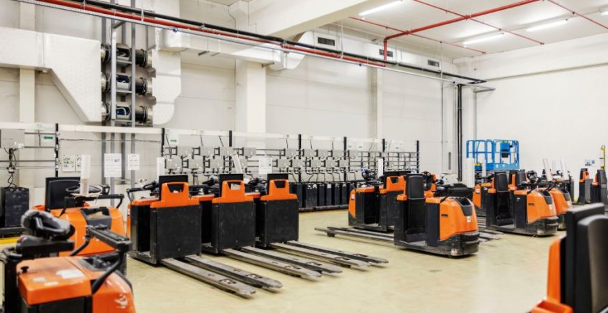 Sala de baterias com empilhadeiras elétricas em armazém, ilustrando a infraestrutura de carga de chumbo-ácido versus a tecnologia de lítio.