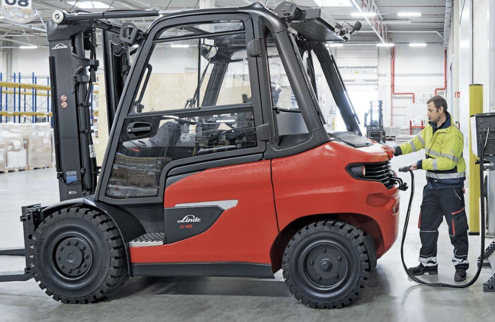 Empilhadeira elétrica conectada ao carregador em armazém logístico, ilustrando a gestão de energia para prolongar a vida útil da bateria e do equipamento.